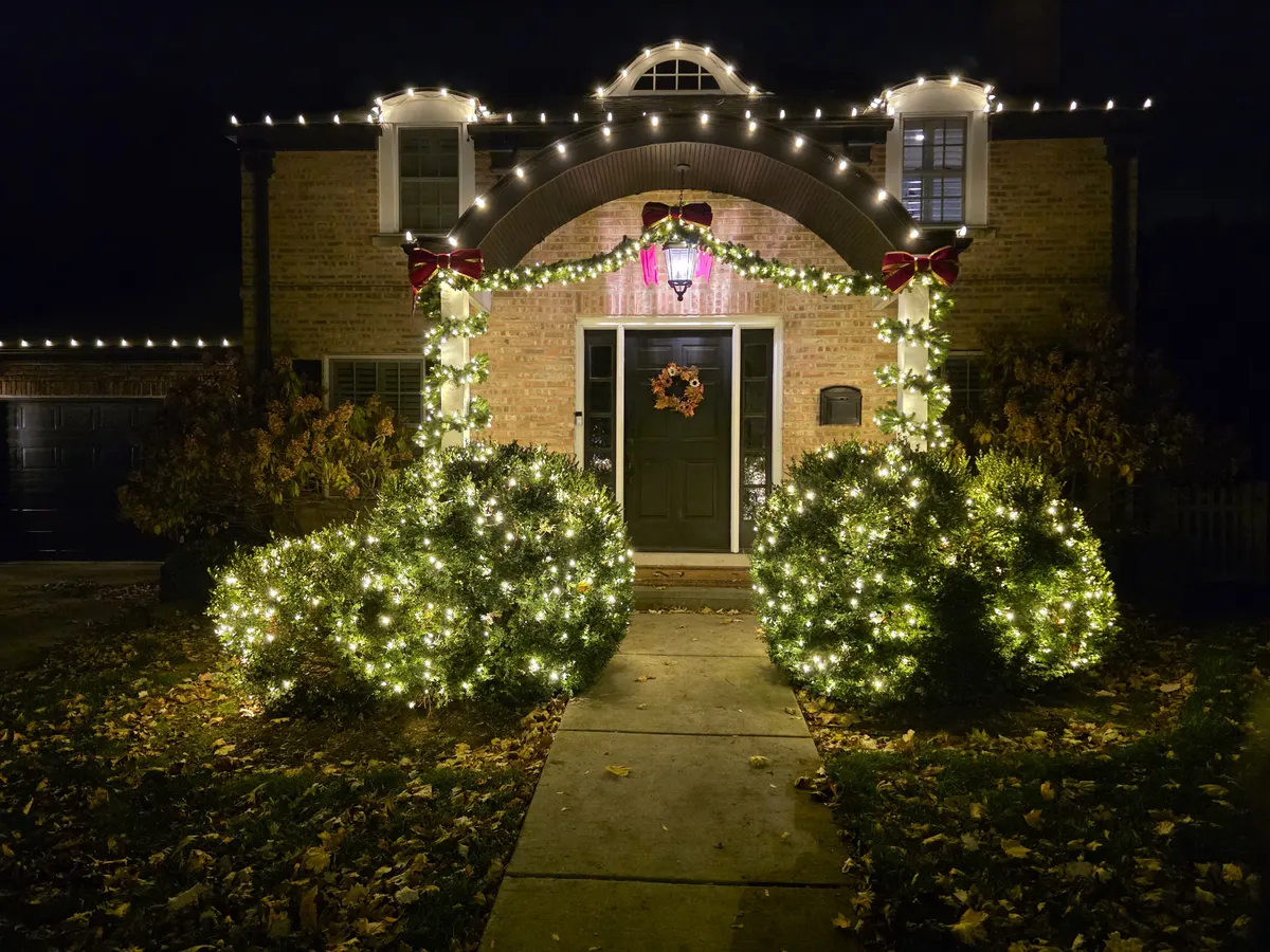 Front entry archway decorated with lit garland and red velvet bows