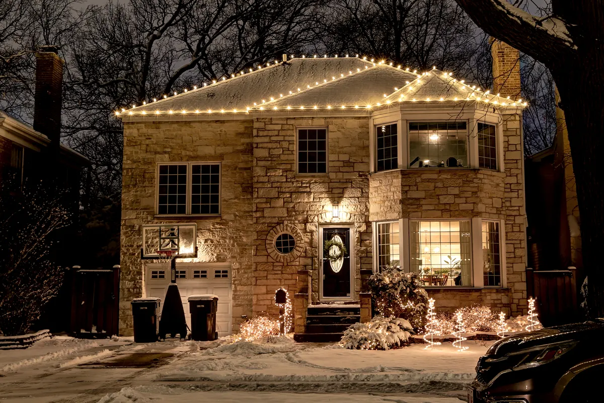 Stone home with warm white roofline Christmas lights and lit bushes at night
